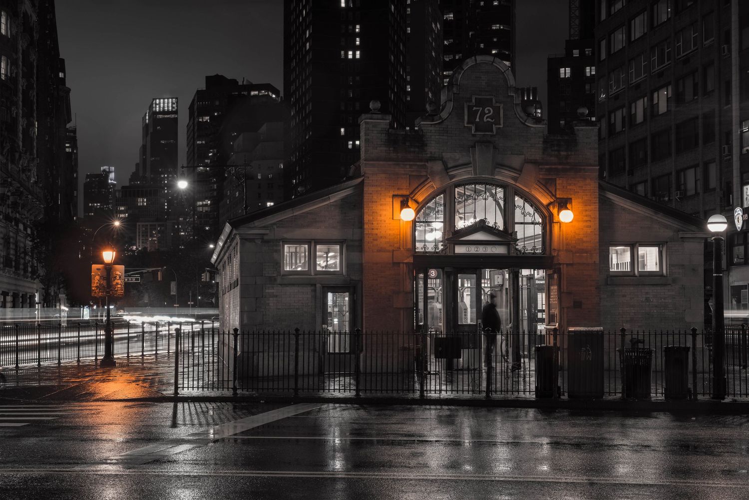 Moody Manhattan nightscape at the 72nd Street Broadway Station with illuminated street lamps casting glow on wet city streets.