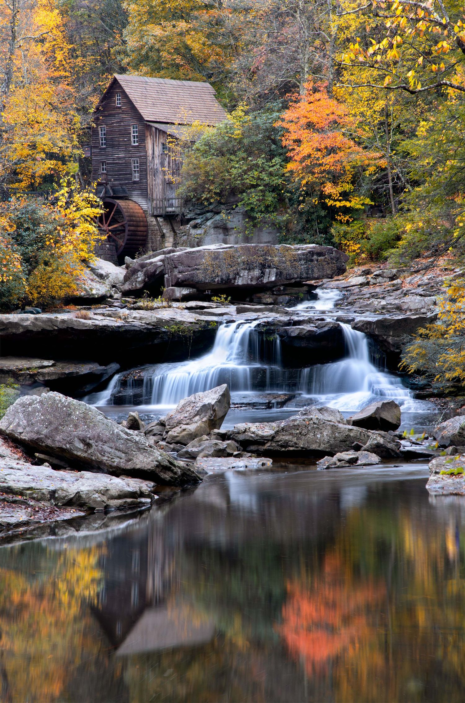 Scenic Glade Creek mill waterfall in West Virginia cascading over rocks with autumn foliage reflected in calm water.