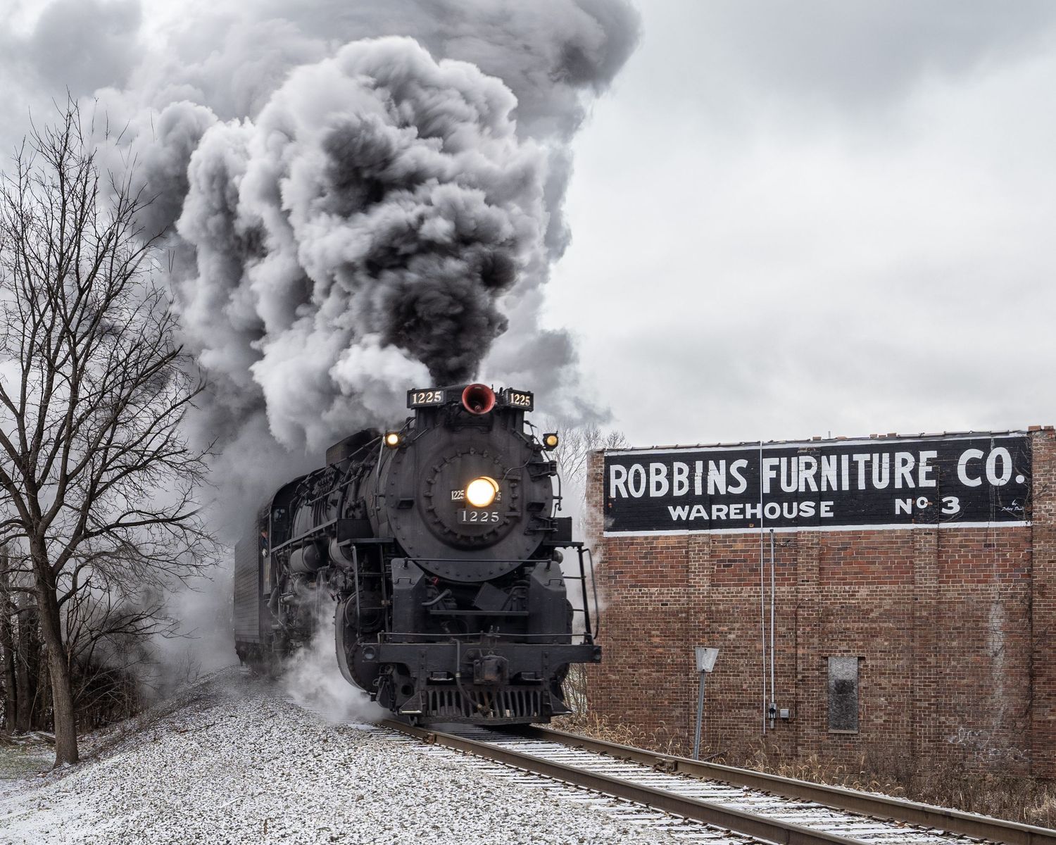 Historic Pere Marquette 1225 steam engine billows steam past Robbins Furniture Co. warehouse building in Owosso, Michigan.