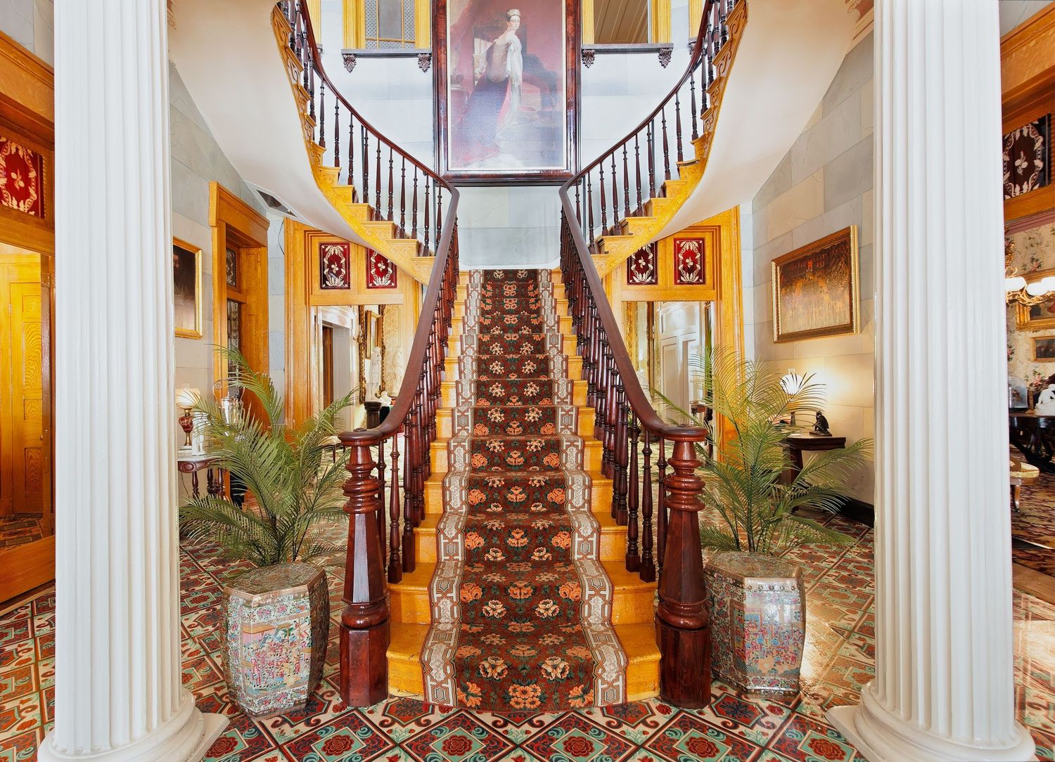 Grand entrance hall with white columns, curved staircase, and ornate Victorian-era decor at the Belmont mansion in Nashville, Tennessee.