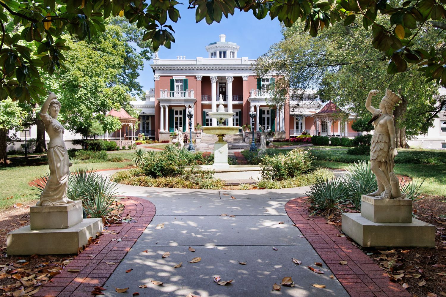 Tree-lined brick pathway with two statues leading to at the Belmont mansion in Nashville, Tennessee on a sunny day.