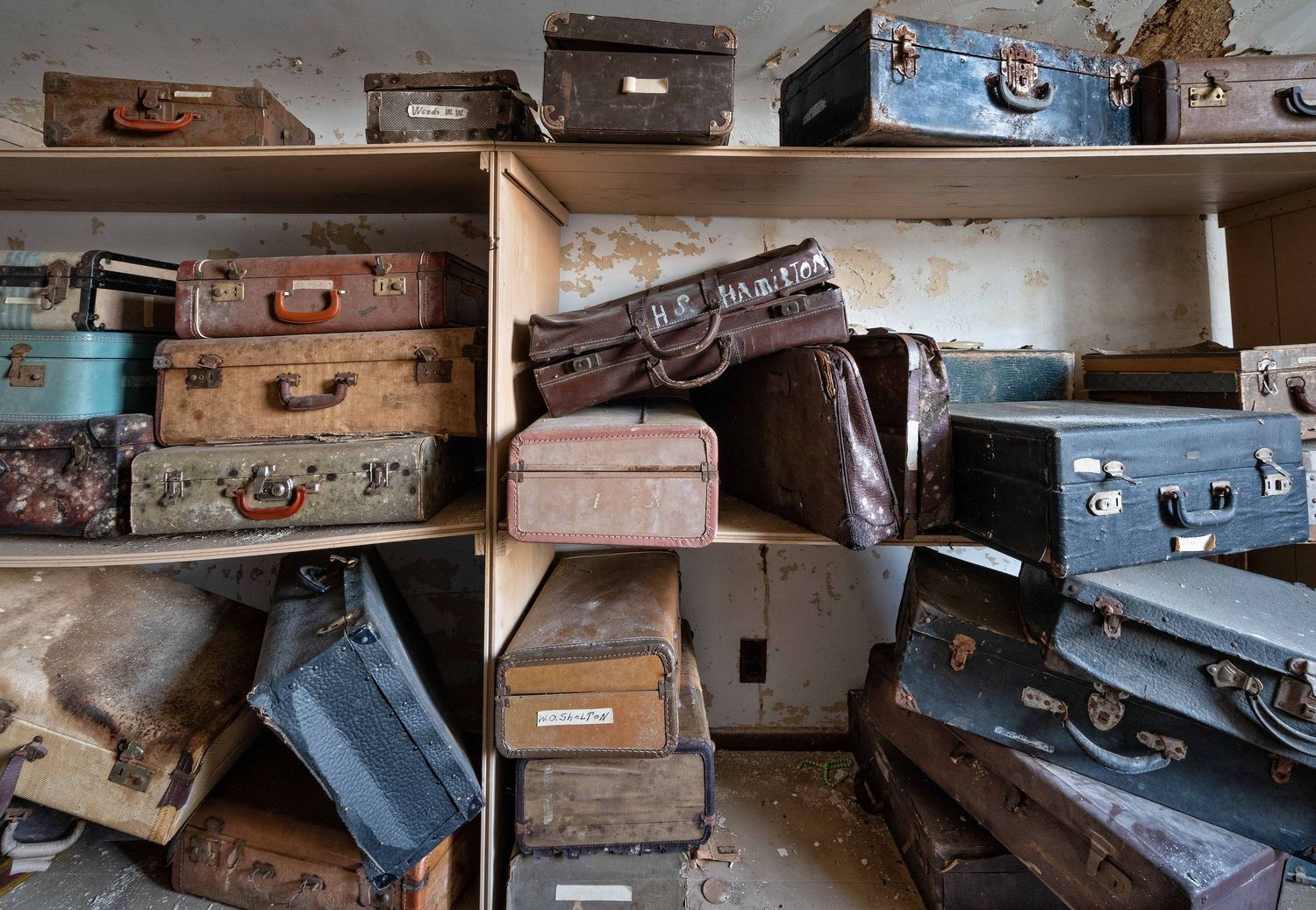 Collection of vintage suitcases and luggage stacked on shelves in an abandoned psych hospital that belonged to patients.