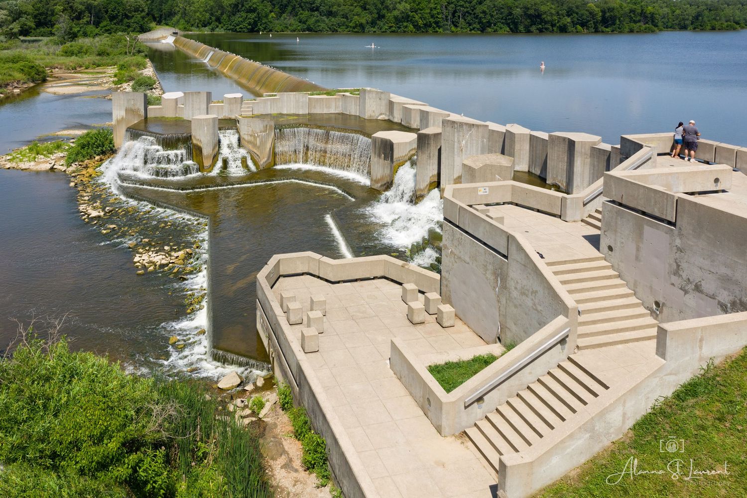 Concrete dam structure with cascading waterfalls and geometric architectural elements along a serene lake at the Flint Stepping Stone Falls.