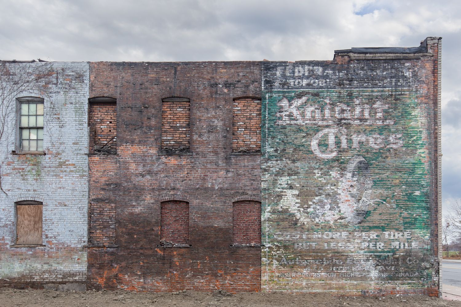 Weathered brick building facade with vintage Knight Tires painted advertisement on deteriorating wall under cloudy sky.