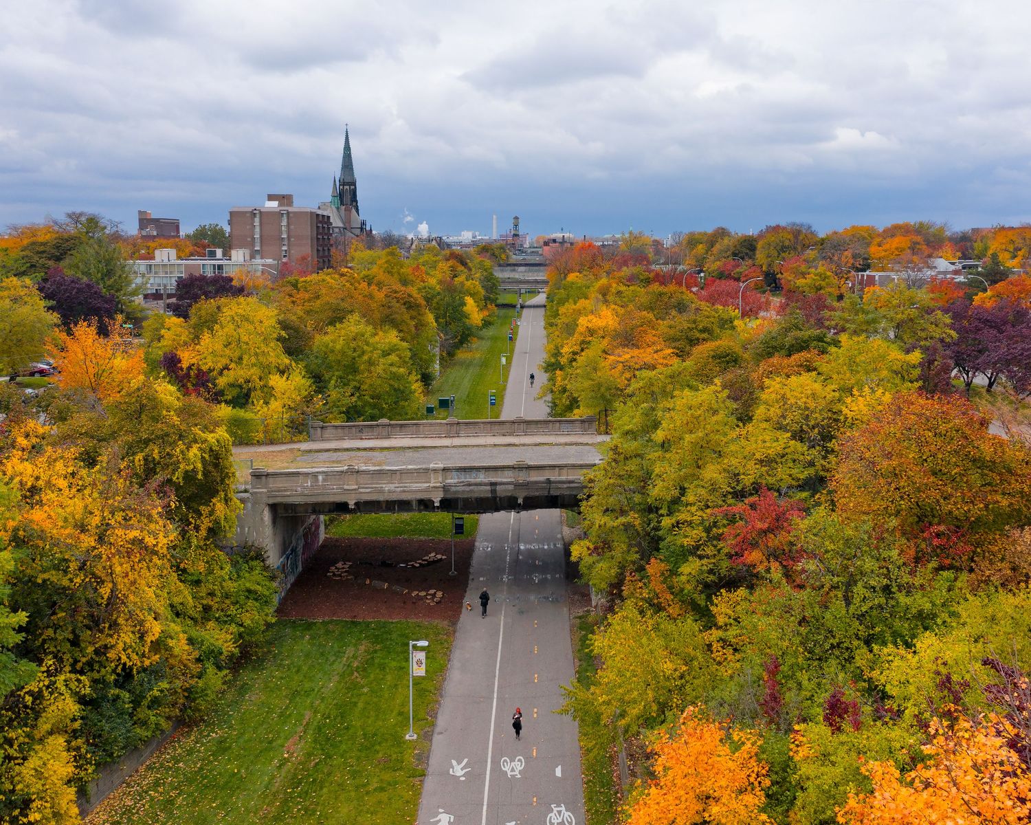 Aerial view of the Dequindre Cut greenway with fall foliage  against an overcast sky with people walking along the path.