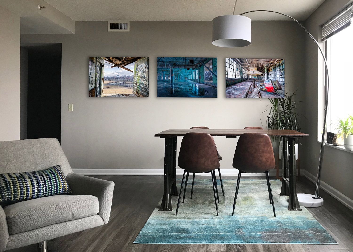 Modern living room with gray furniture, blue area rug, and contemporary decor with three photos of Detroit hanging on the wall.