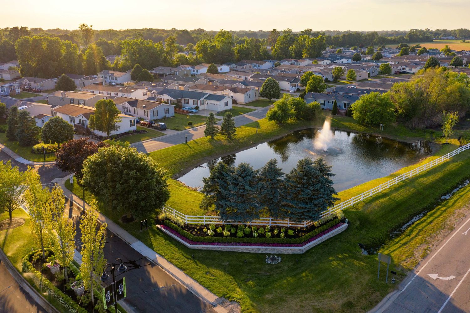 Aerial panoramic view of Augusta Woods manufactured homes community with houses and pond during golden sunset in Wilis, Michigan.