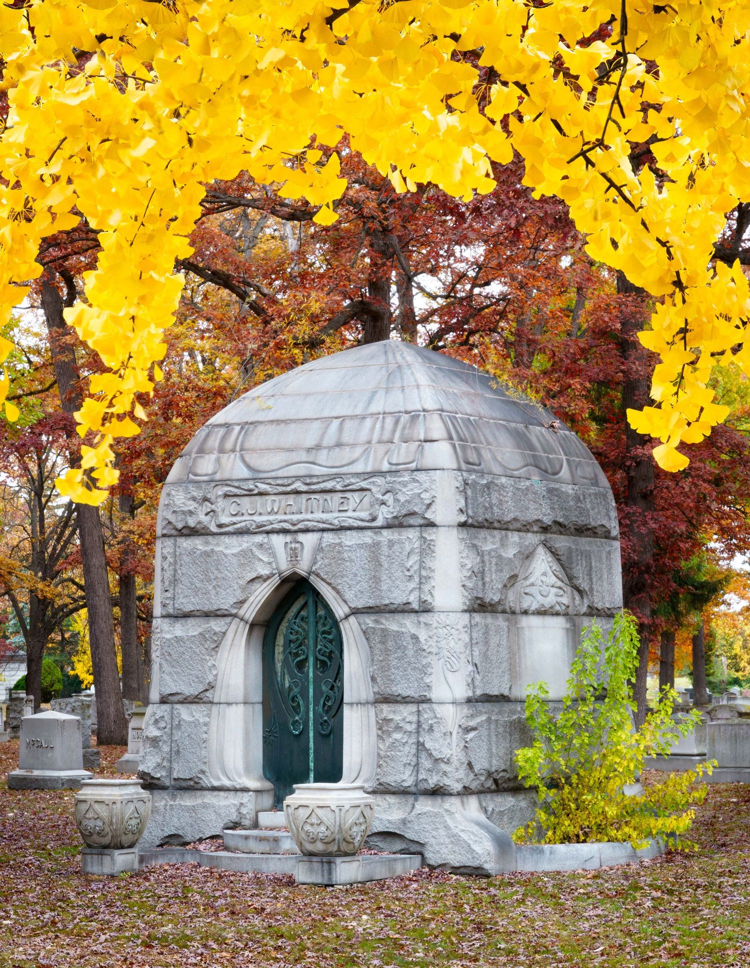 CJ Whitney mausoleum with a green art deco door surrounded by yellow Gingko tree leaves in historic Woodlawn cemetery in Detroit.