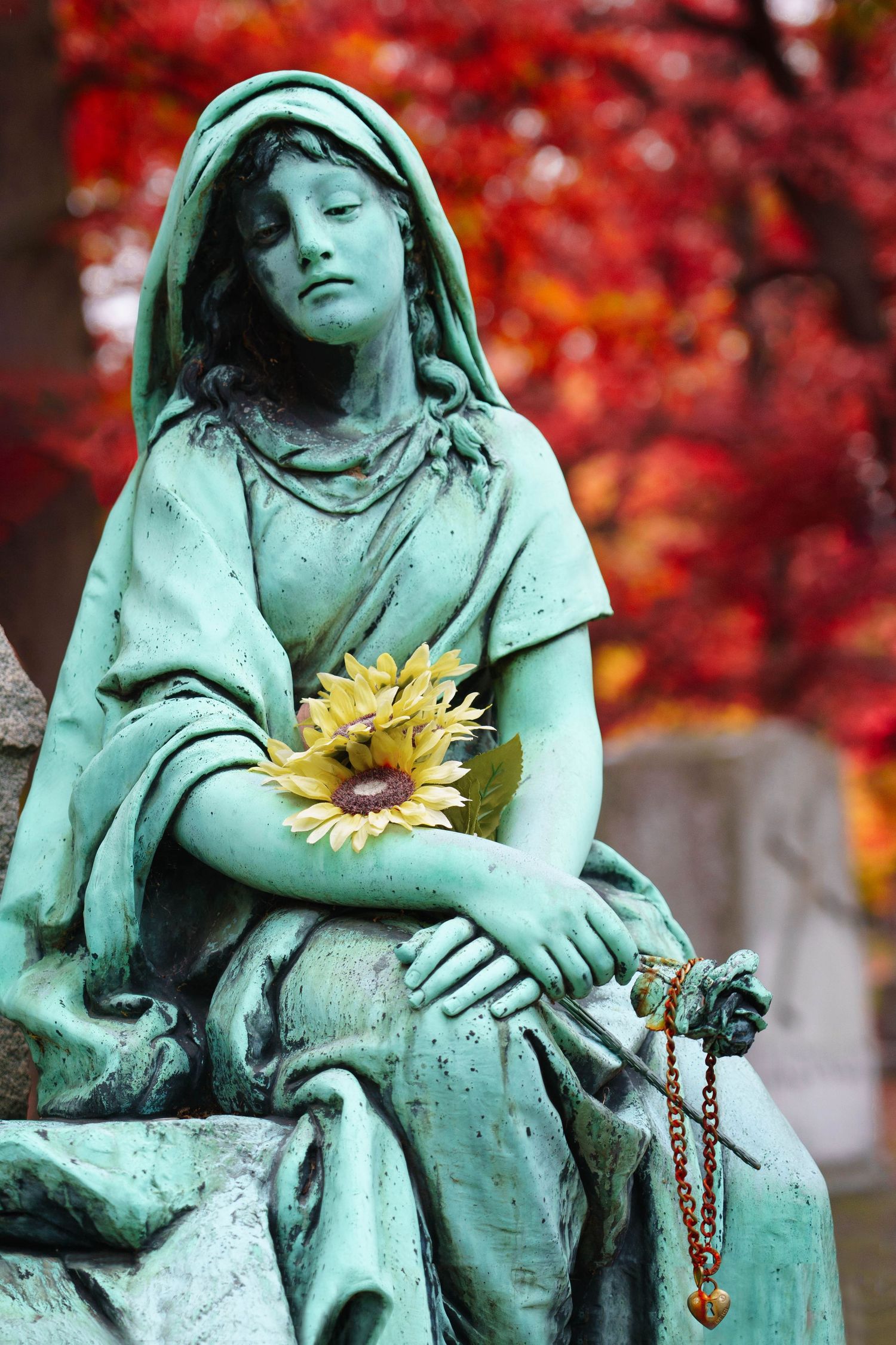 Patinated bronze cemetery statue with a sunflower against vivid red autumn foliage background at Woodlawn cemetery in Detroit, Michigan.