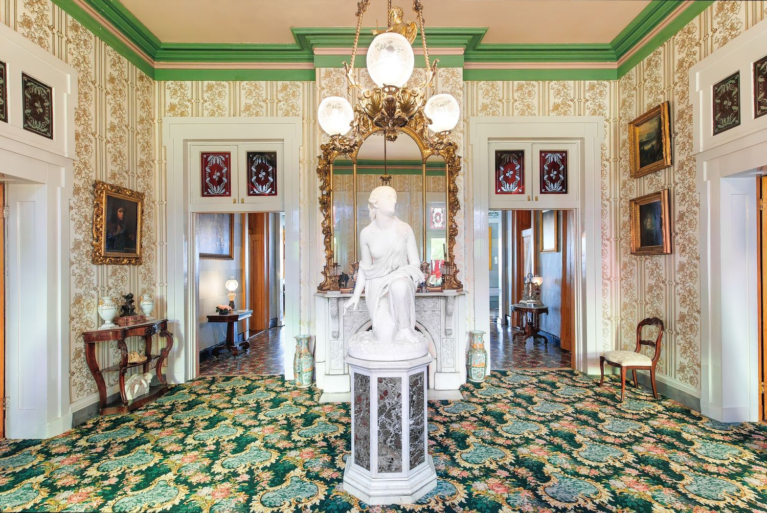 Ornate entrance with green trim, vintage wallpaper, and antique furnishings with statue at the Belmont mansion in Nashville, Tennessee.