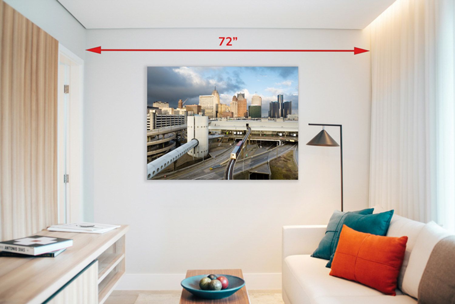 Modern white living room interior with white couch, teal and orange accent pillows with an image of downtown Detroit, Michigan on the wall.