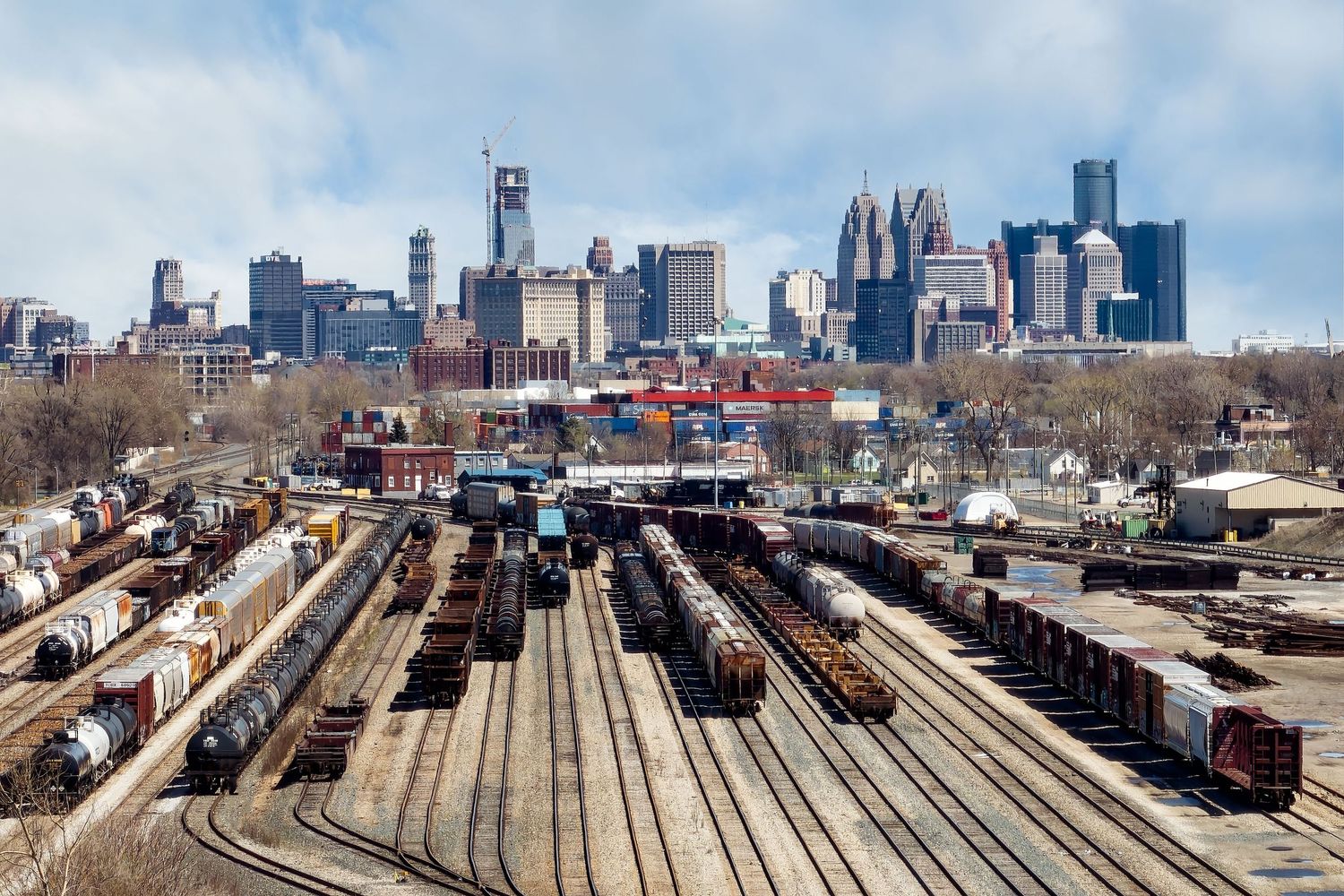View of an urban railroad yard with the Detroit skyline in background.