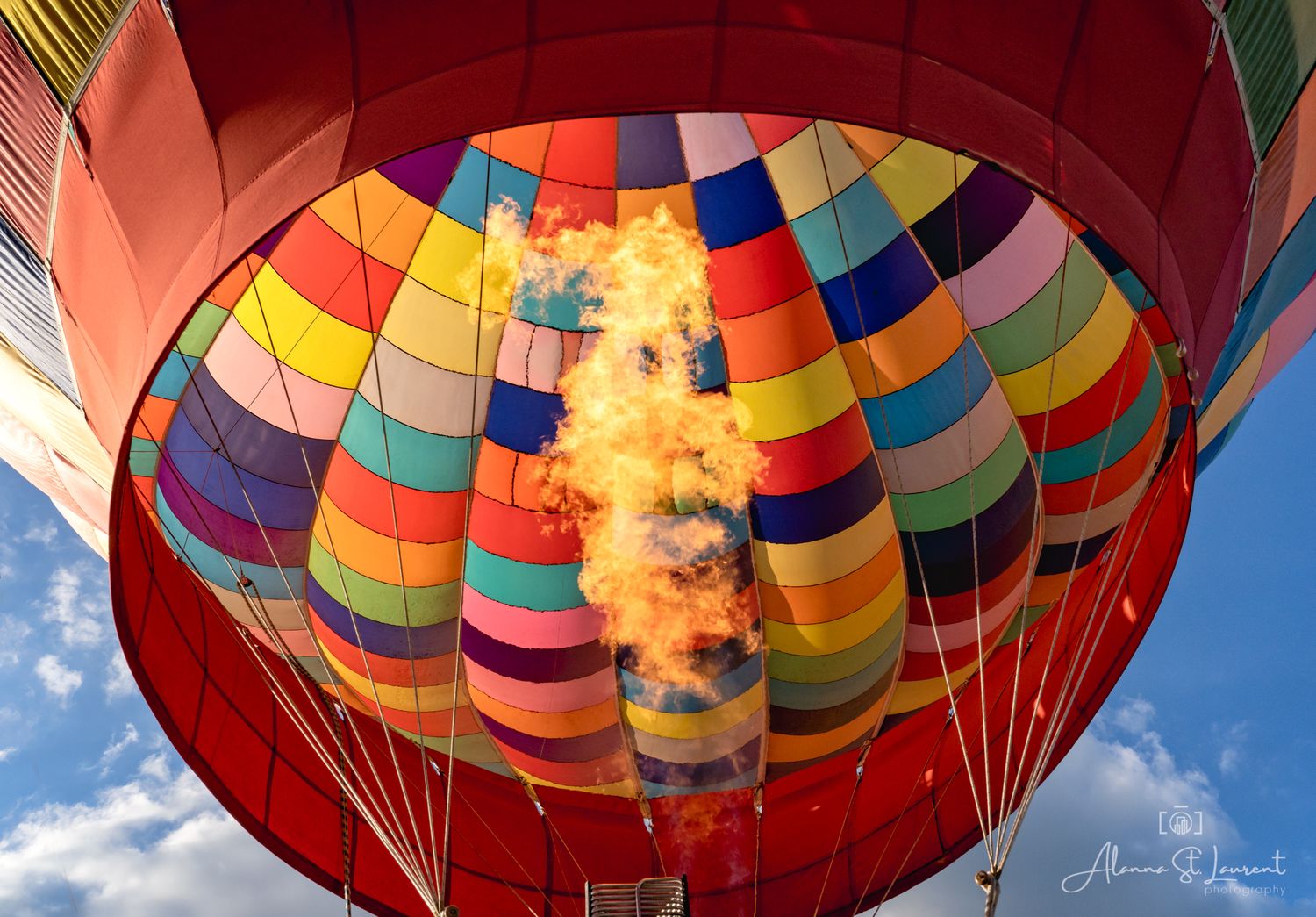 Colorful hot air balloon glowing with flames against a blue sky during the Metamora Hot Air Balloon festival in Metamora, Michigan.