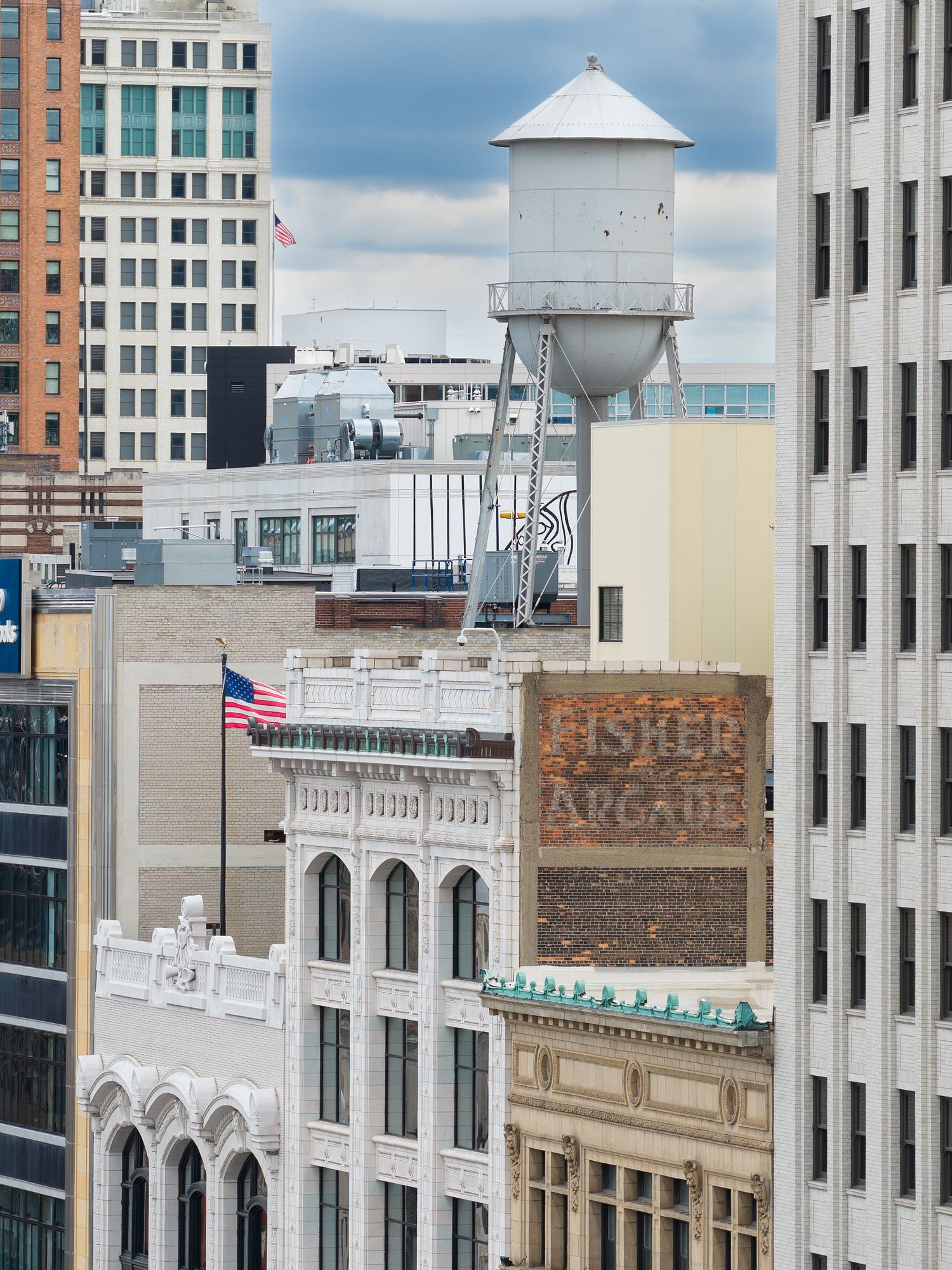 Rooftop view of historic brick buildings with architectural details and a water tower against a cloudy sky in downtown Detroit Michigan.