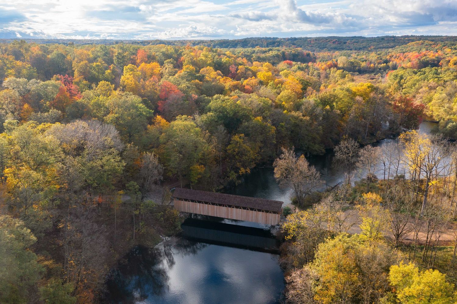 Aerial of the Whites covered bridge in autumn showing winding Flat river through colorful fall foliage.