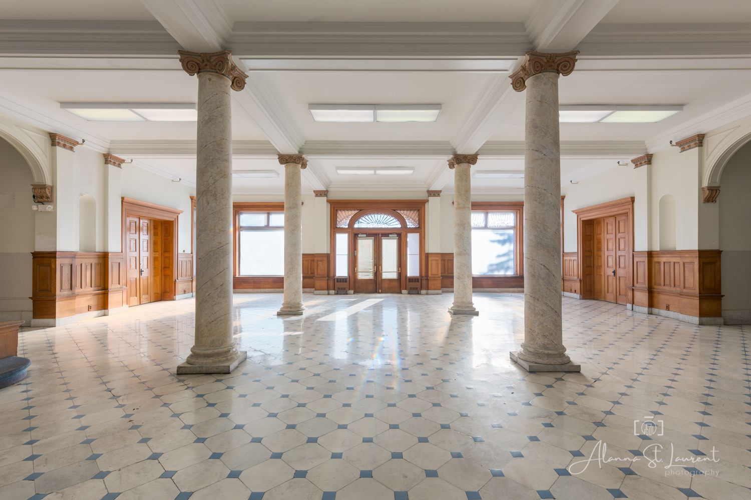 Grand historic building interior with marble columns, ornate tile floors, and elegant wooden doors in a spacious lobby.