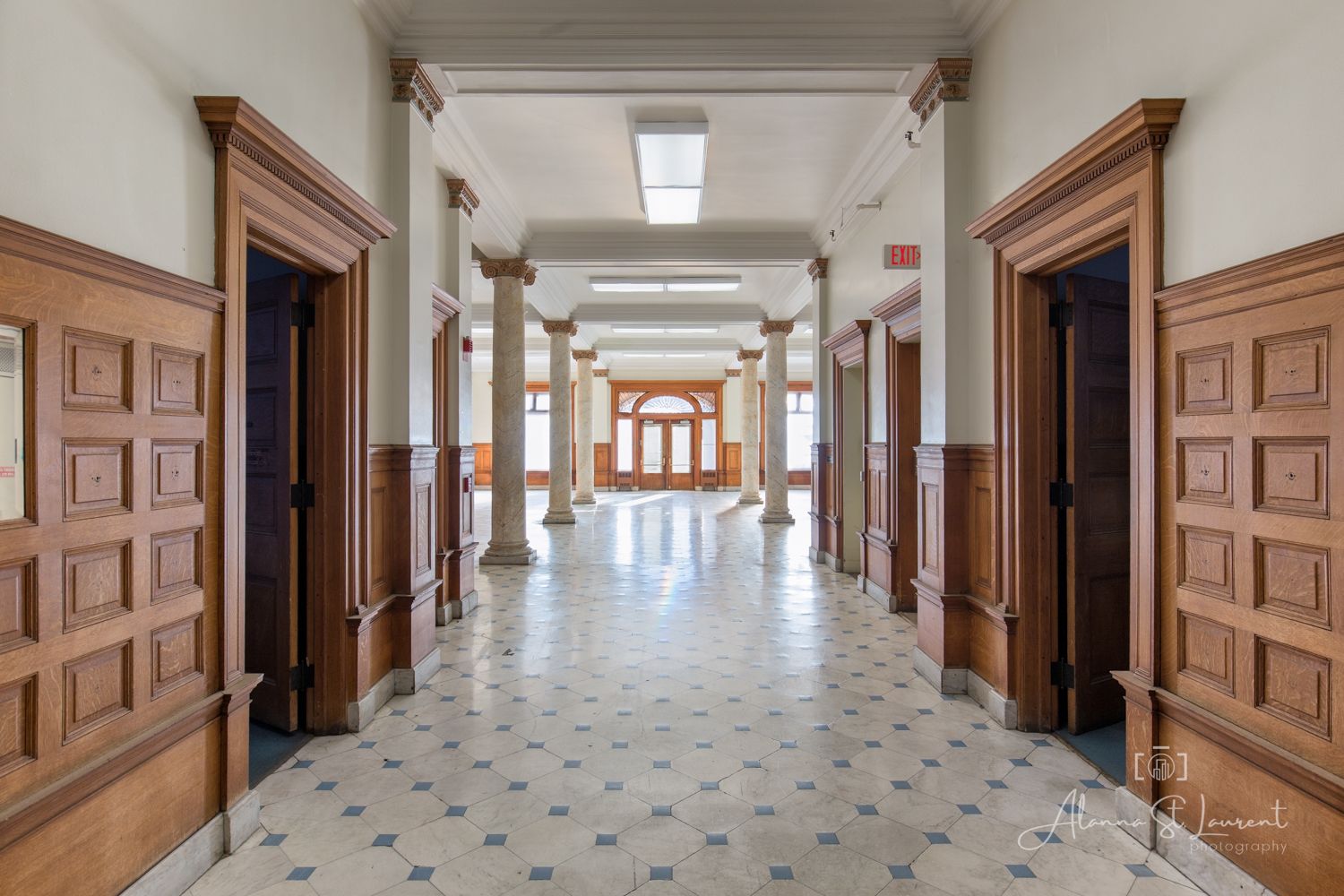 Elegant hallway with rich wood paneling, ornate columns, and classic checkered tile flooring in a historic building.