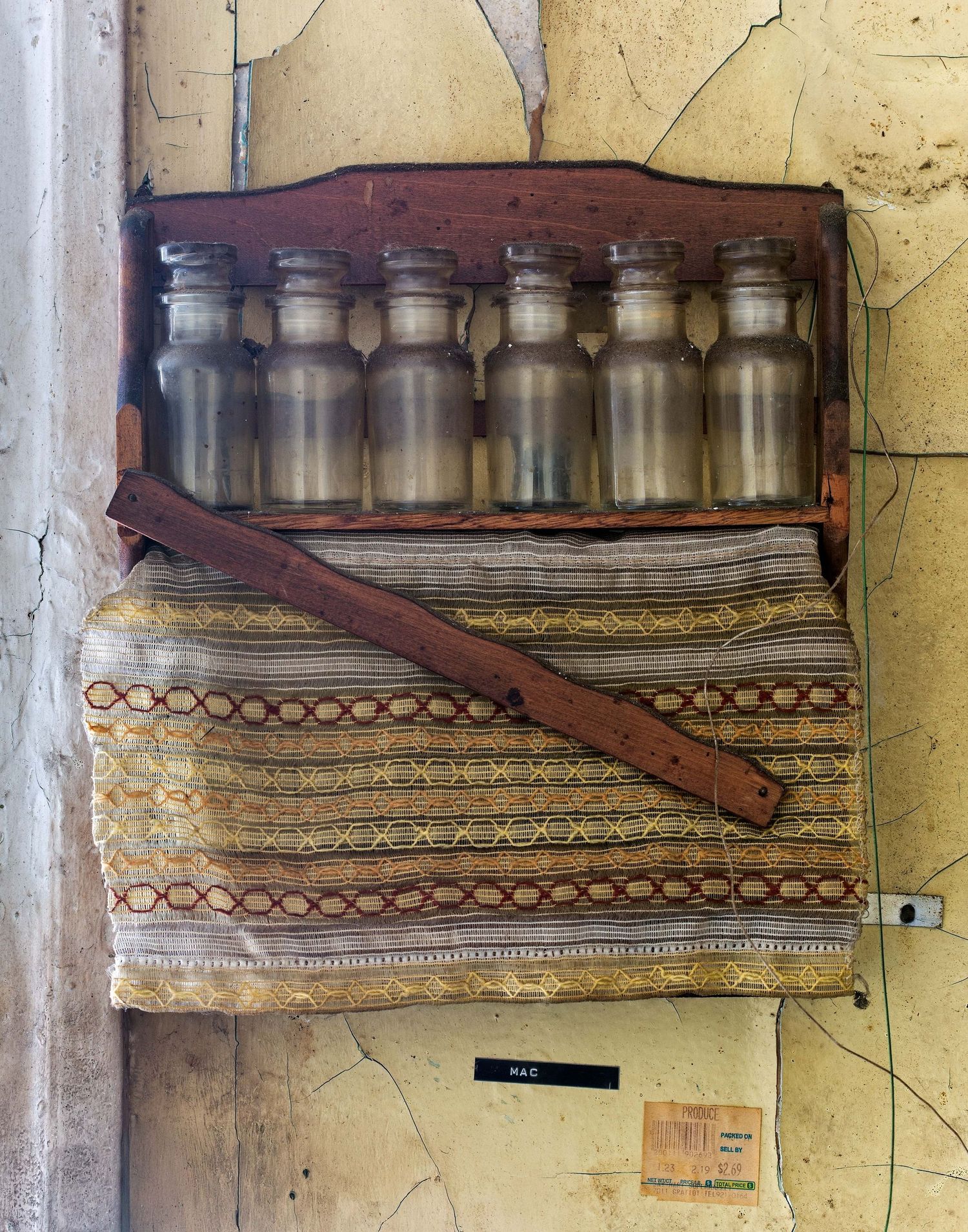 A falling apart shelf displaying spice jars against a weathered yellow wall in a kitchen of an abandoned home in Detroit, Michigan.