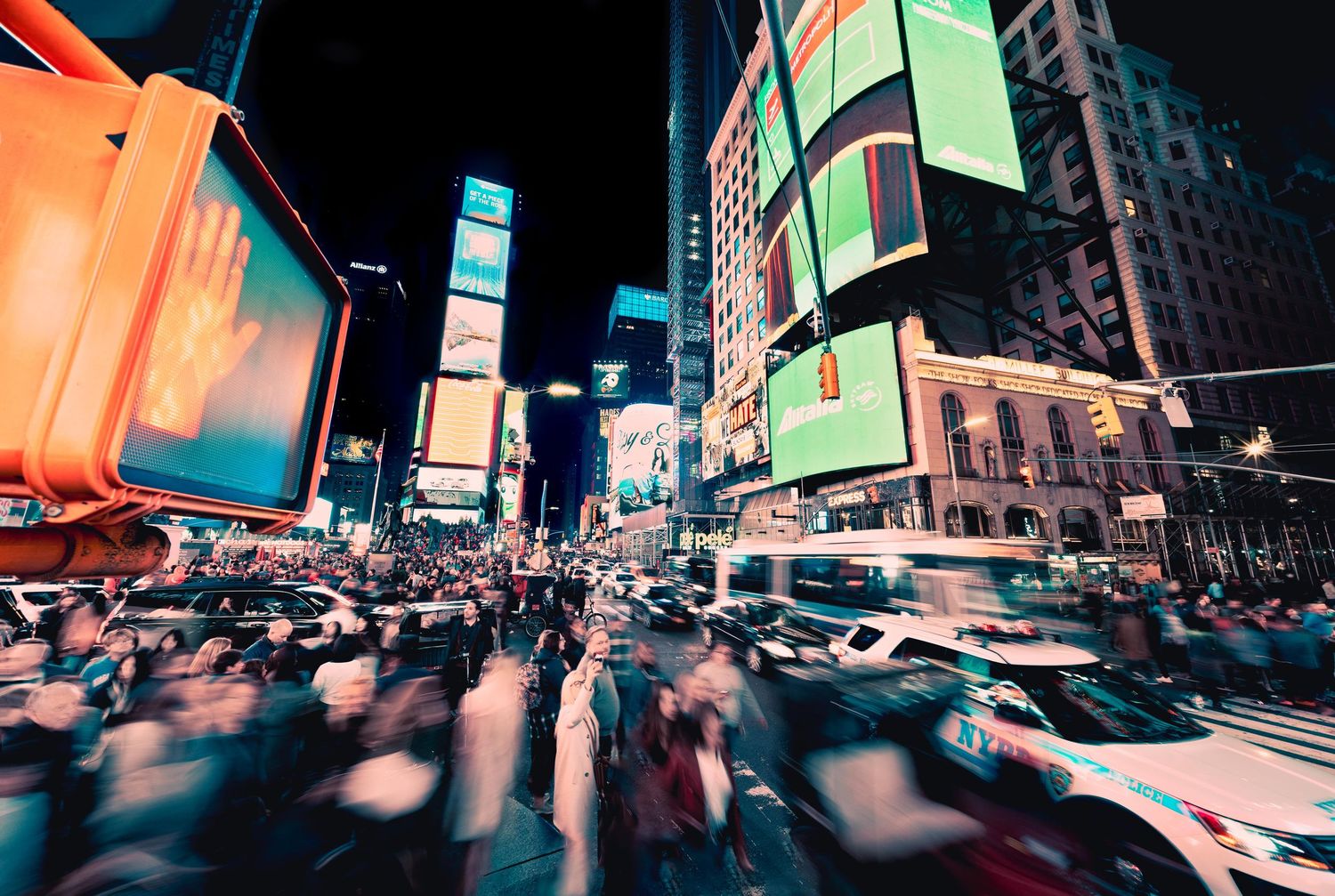 Manhattan Times Square at night with motion-blurred yellow taxis against neon-lit buildings and blurred people moving through.