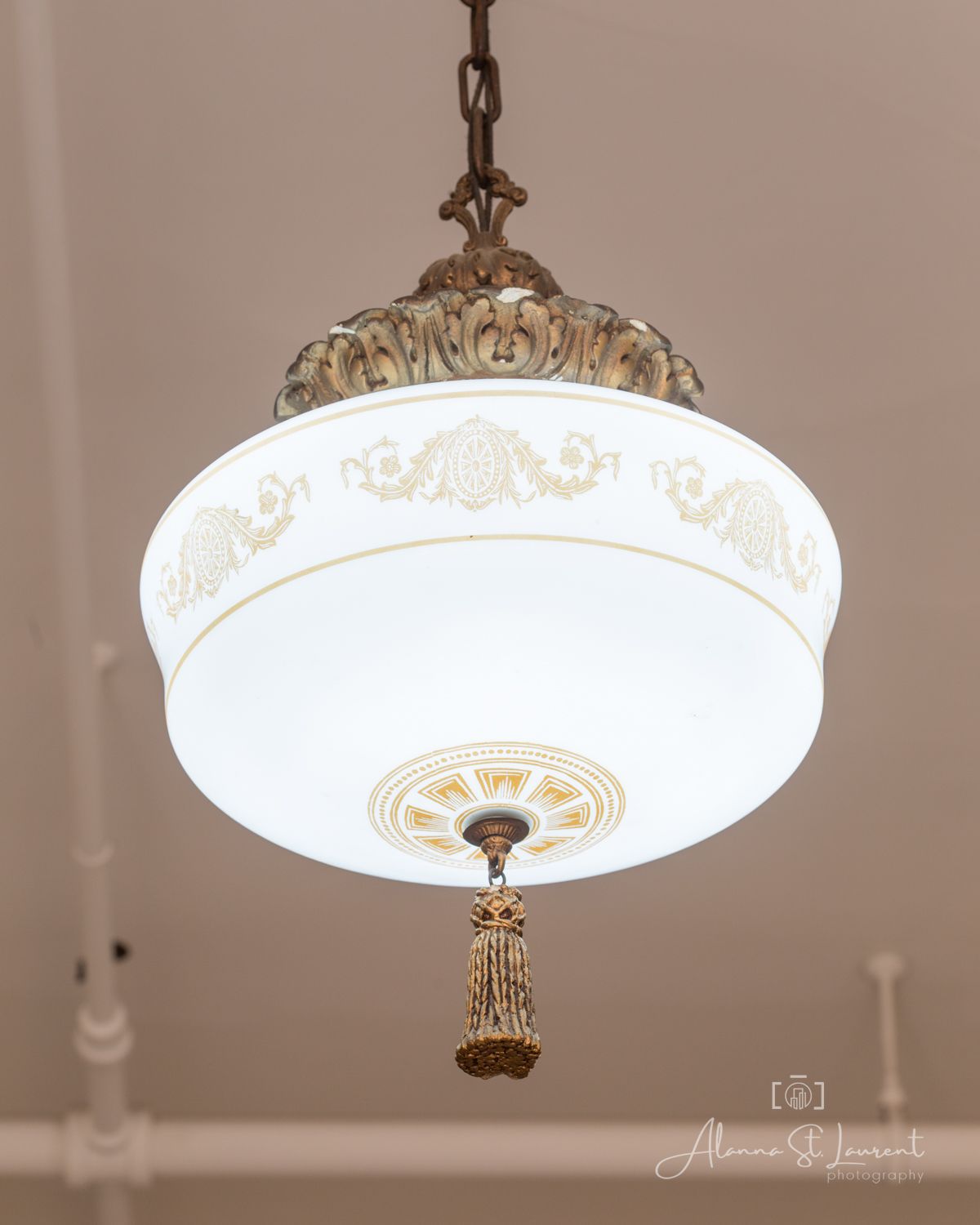 Vintage brass pendant light with ornate frosted glass globe shade, gold floral motifs, and decorative tassel pull chain.