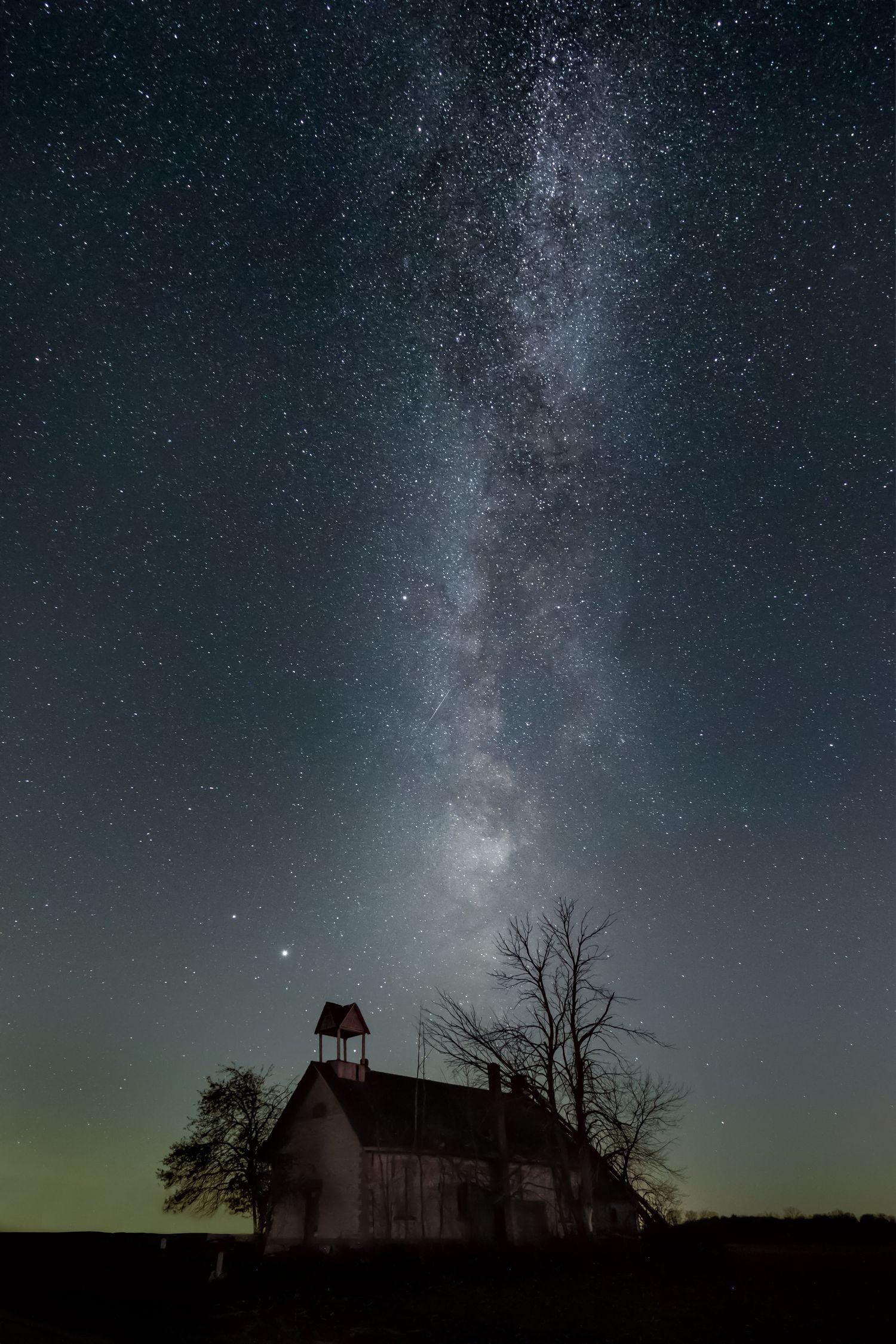 Milky Way galaxy stretching across dark night sky over an abandoned schoolhouse in the Thumb area of Michigan.