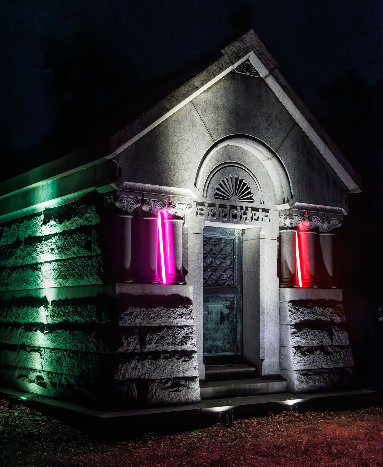 Stone mausoleum exterior dramatically lit with green and pink accent lighting at night at the Elmwood Cemetery in Detroit, Michigan.
