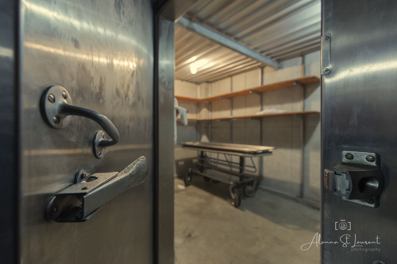 Metal vault door open revealing a small storage room with wooden shelves and a workbench inside.