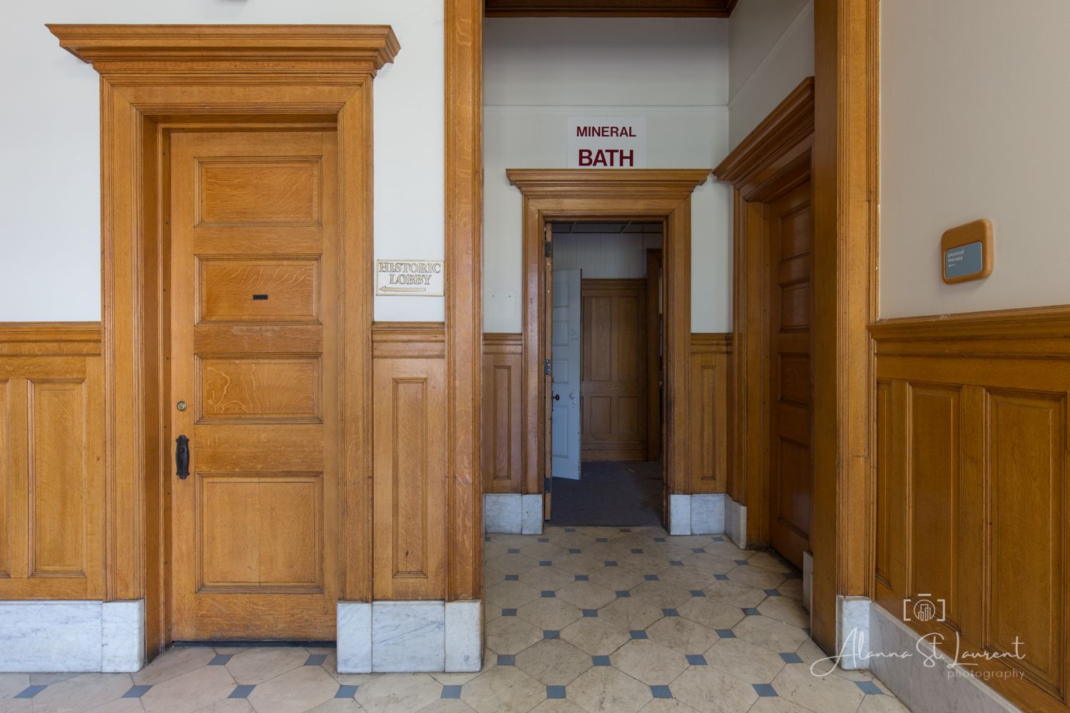 Historic wooden doors and wainscoting in an elegant hallway leading to a Mineral Bath room with ornate tile flooring.
