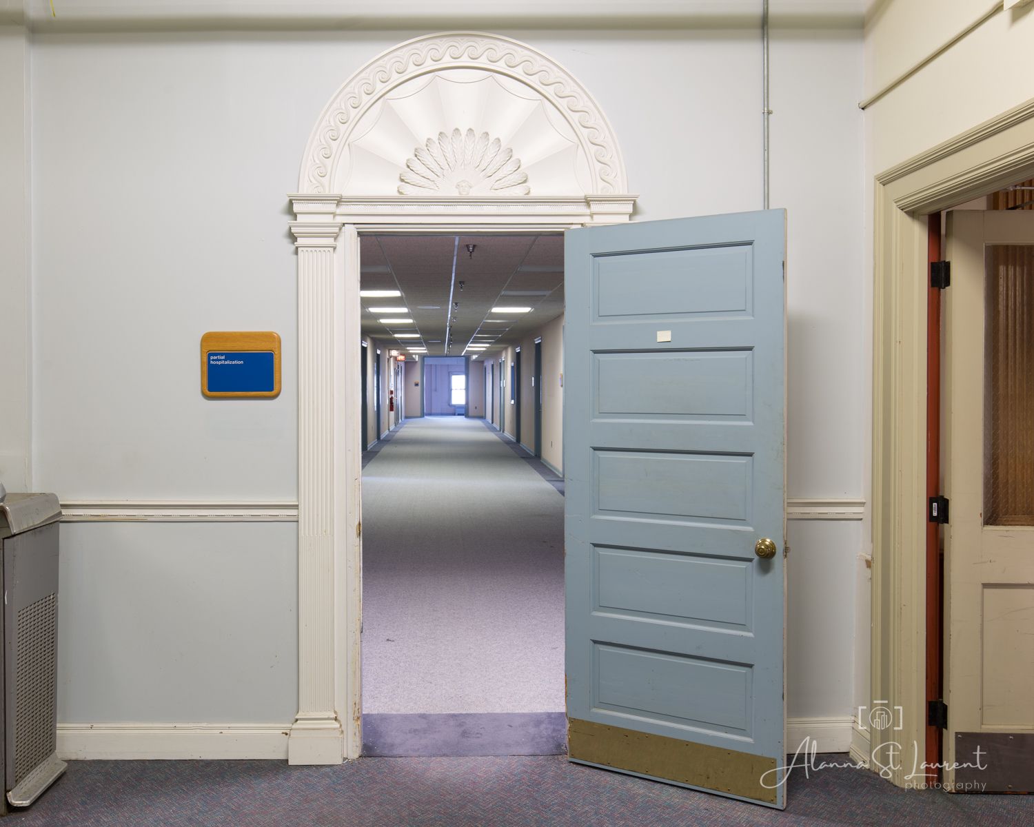 Open blue door leading into a long hallway with purple carpet in a classic building with ornate white doorframe.