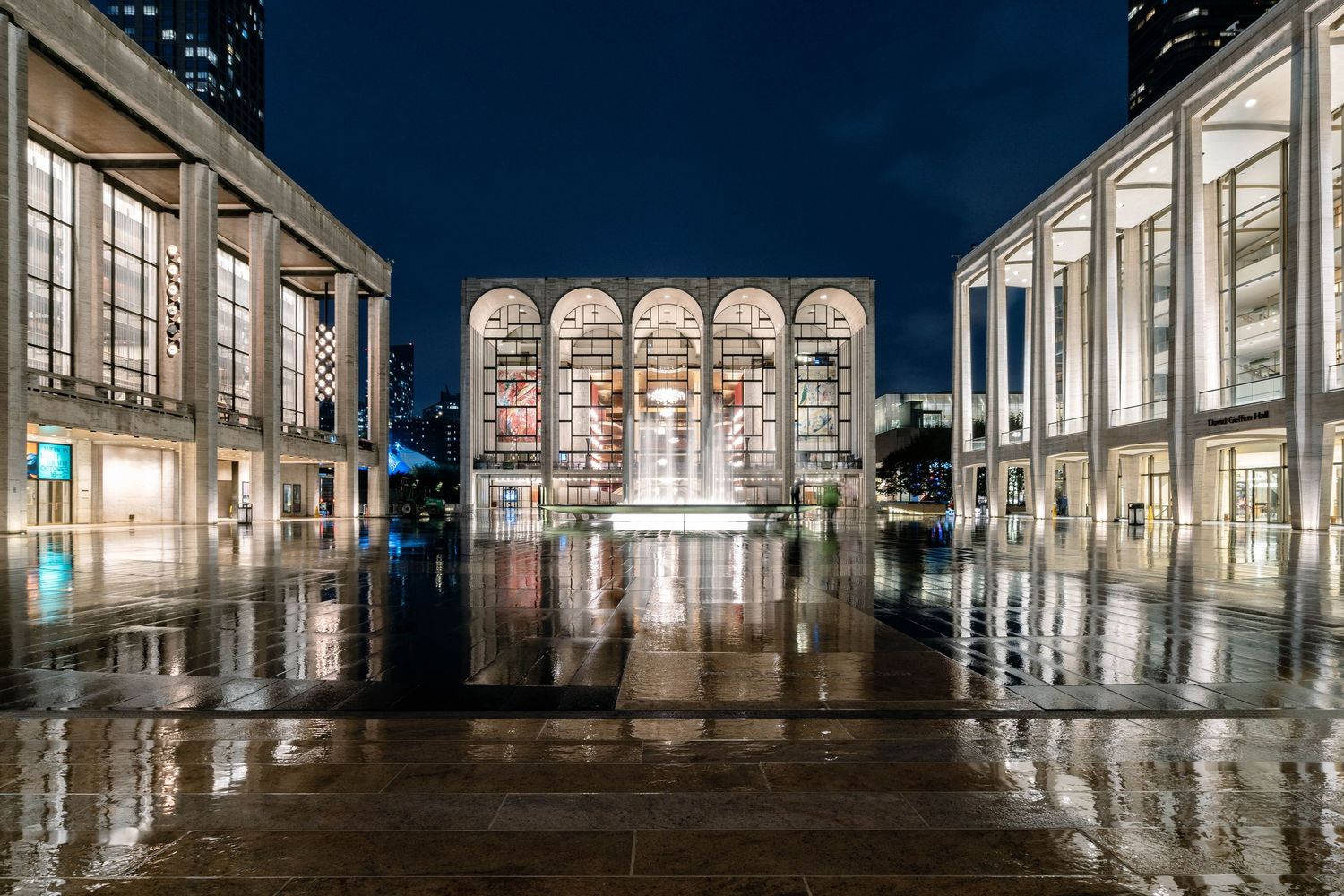 Manhattan Lincoln Center at night with reflections from wet pavement.
