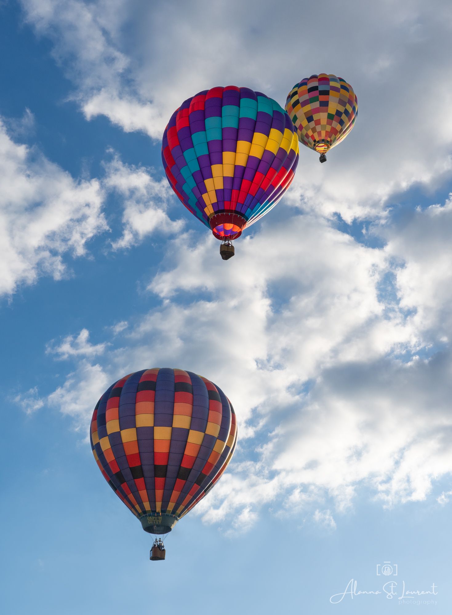 Multiple colorful hot air balloons soaring through white clouds against bright blue sky in Metamora, Michigan.