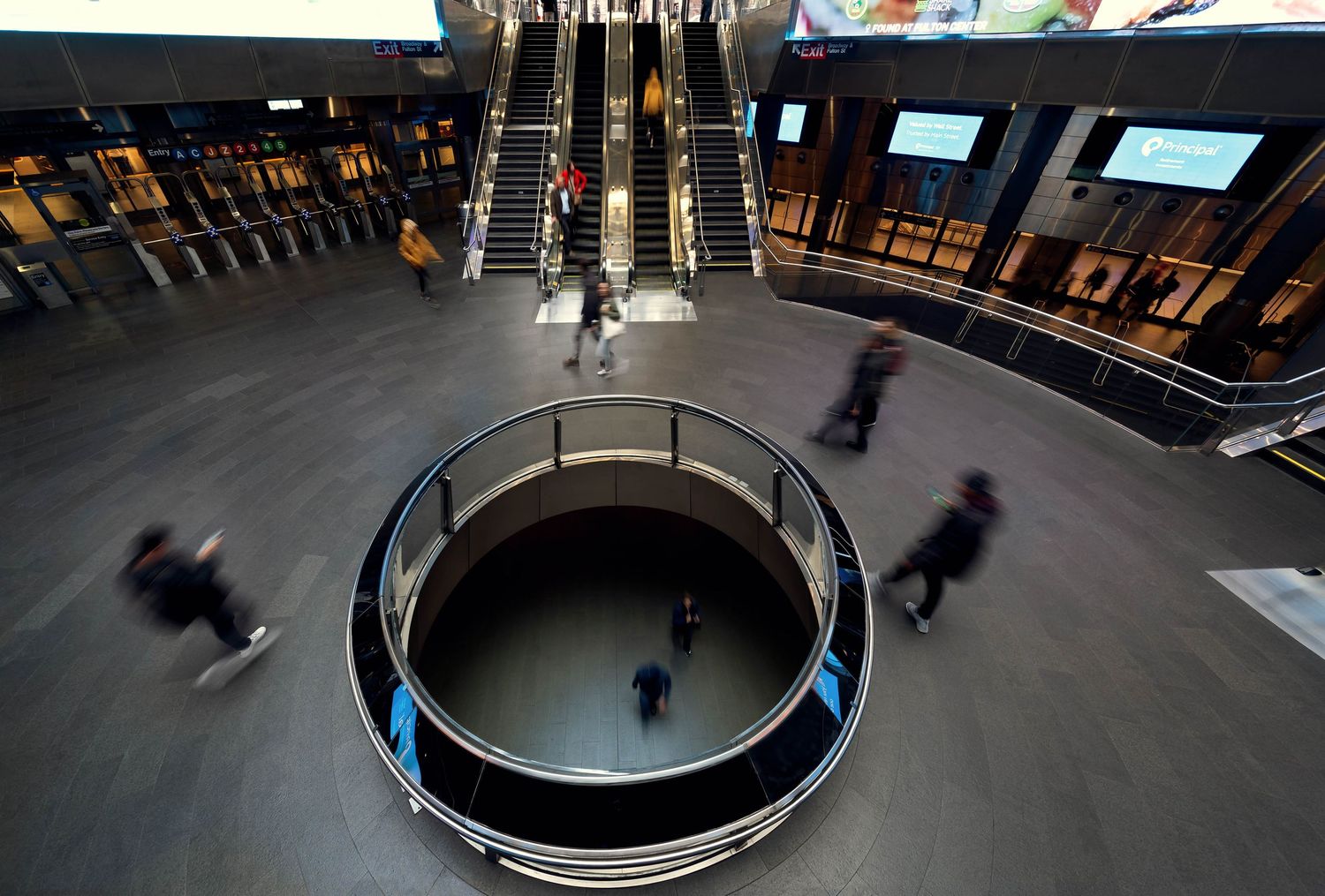 Manhattan Fulton Street subway station with blurred human figures moving through towards their destinations.