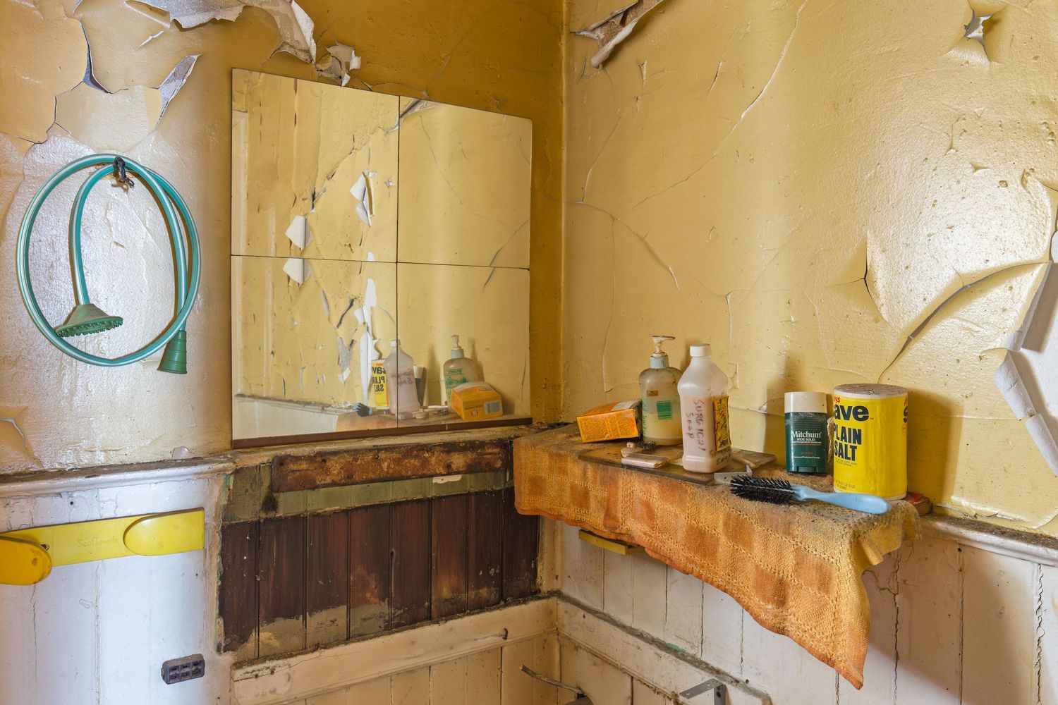 Old yellow wall with peeling paint shows signs of deterioration and age in a bathroom of an abandoned home in Detroit, Michigan.