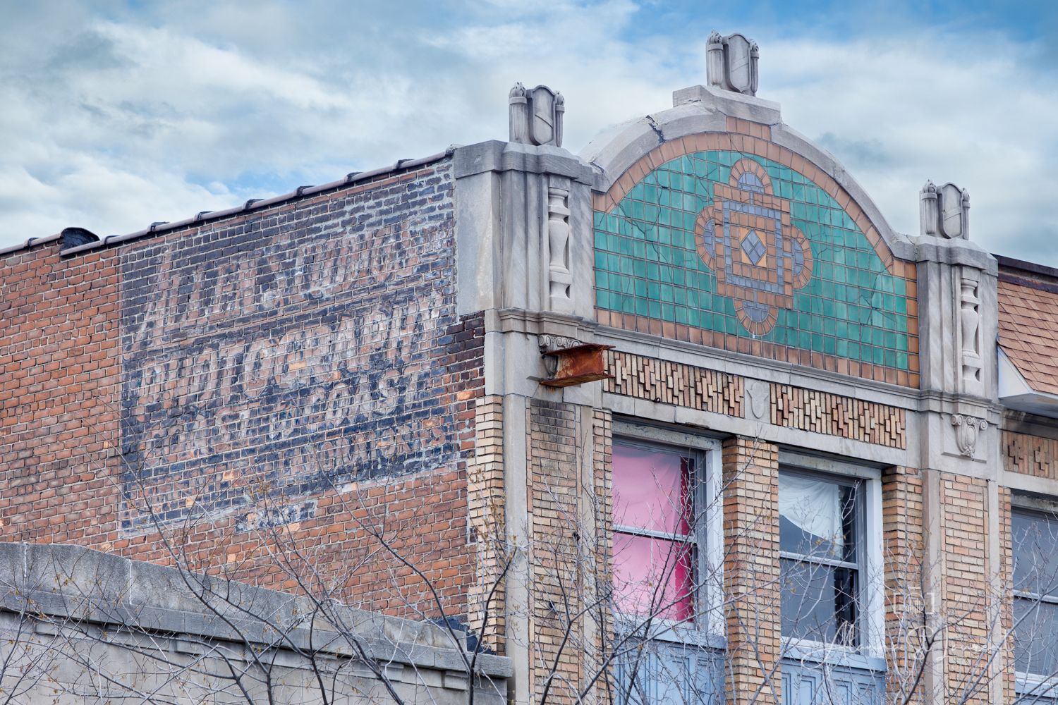 Vintage brick building with faded ghost sign reading Photography Coast to Coast and ornate tiled facade under cloudy sky.