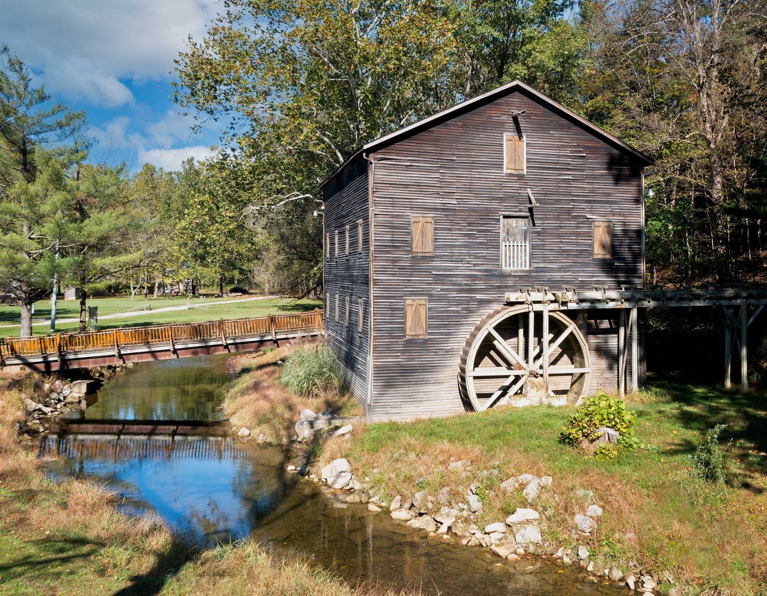 Historic Wolf Creek mill with large wheel beside a peaceful creek surrounded by trees.