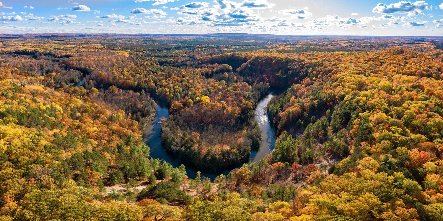 Aerial panorama of the Manistee river through vibrant autumn forest and blue skies at the High Rollway Scenic Overlook in Kingsley, MI.