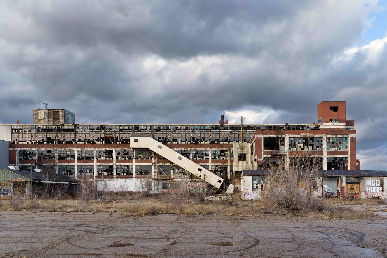 Panoramic view of the Cadillac Stamping plant with broken windows and exposed structural elements against cloudy skies in Detroit, Michigan.