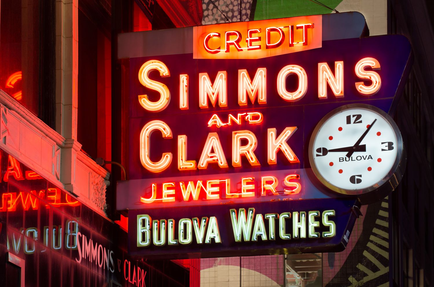 Vintage neon sign for Simmons and Clark Jewelers featuring Bulova Watches clock at night.