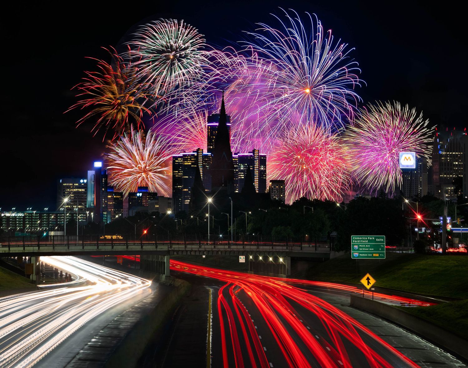 Colorful fireworks display over the Detroit skyline with traffic light trails from I-75 traffic in foreground captured by Alanna St Laurent.