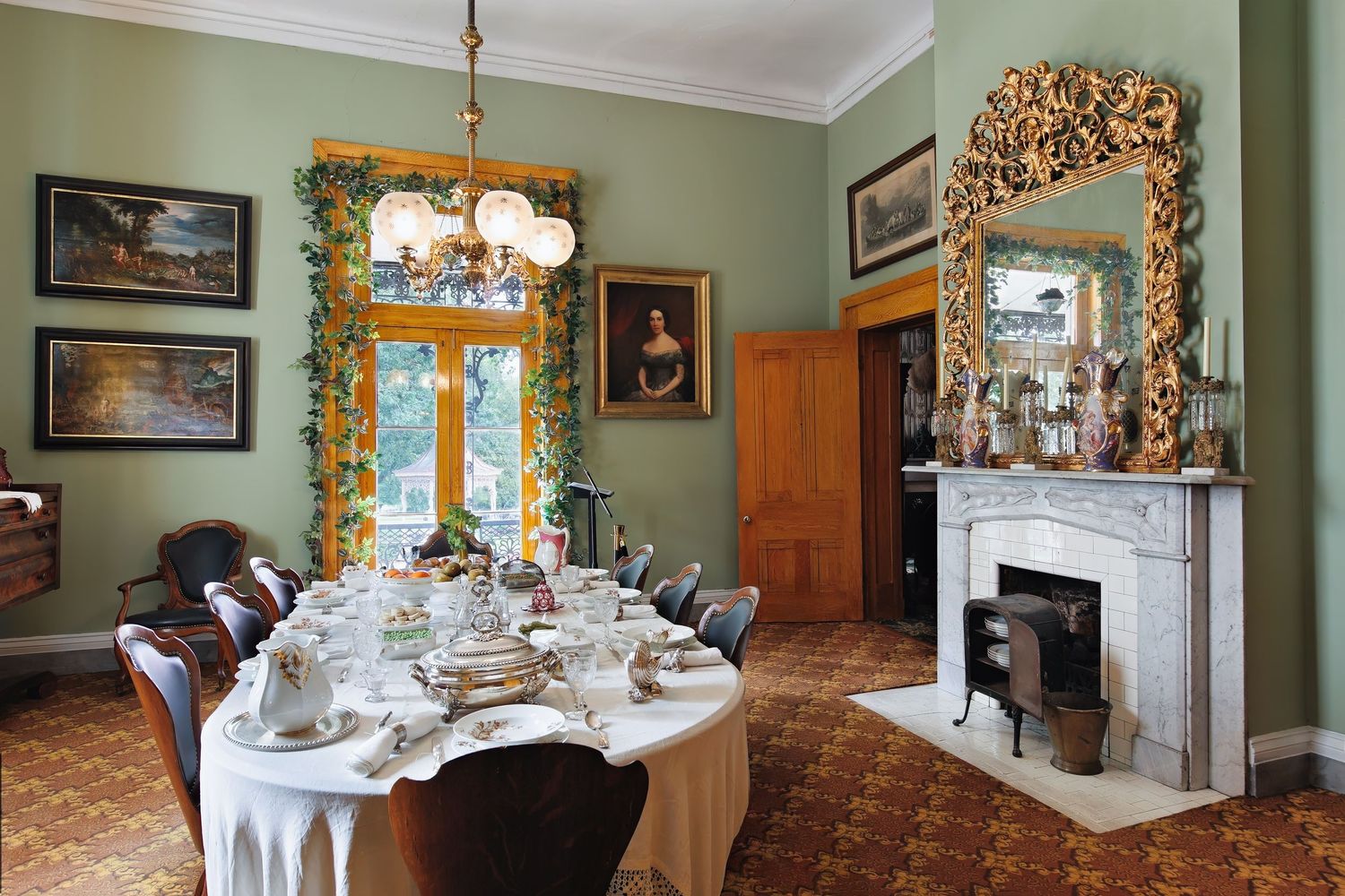 Dining room with green walls, gold-framed artwork, and elegant table settings at the historic Belmont mansion in Nashville, Tennessee.