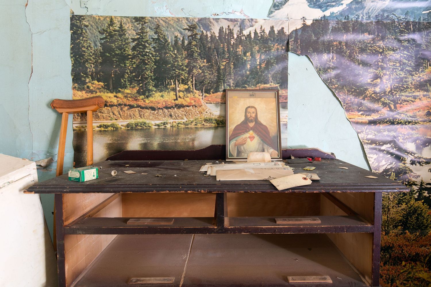 A bedroom with a framed photo of Jesus with peeling wallpaper in an abandoned home in Detroit, Michigan.