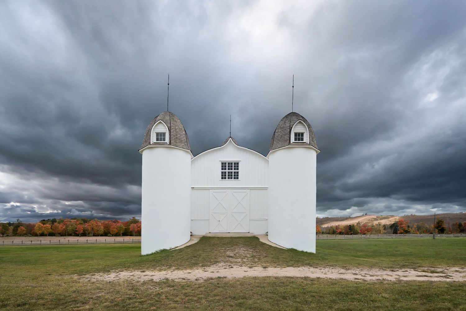 DH Day barn with twin spires stands against moody storm clouds and fall colors in Michigan.