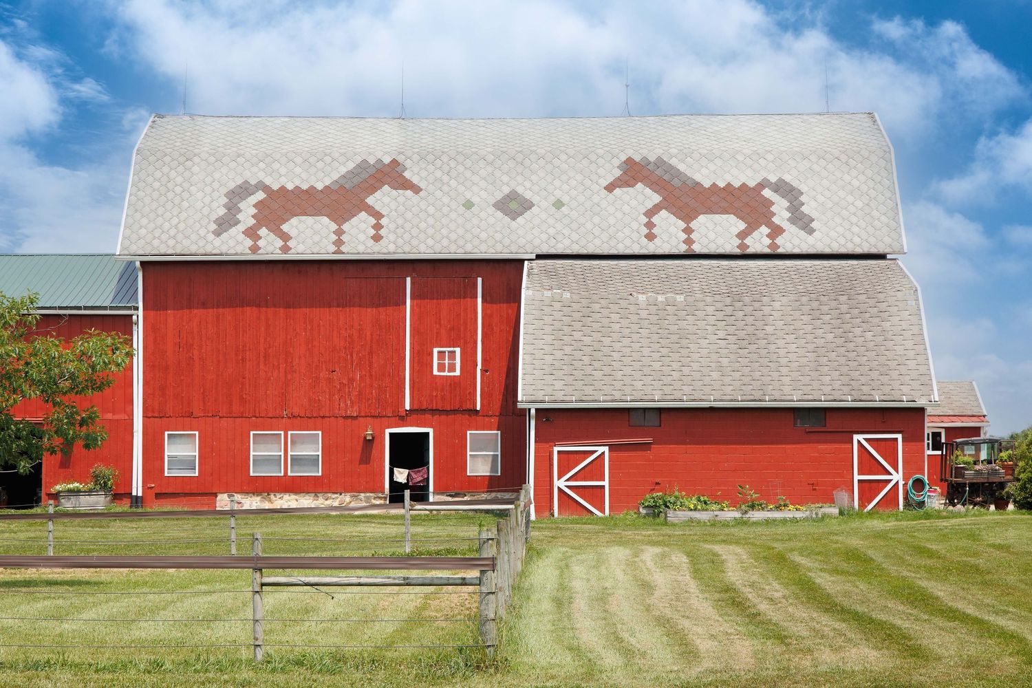 A red wooden barn in Saline Michigan with white trim set against a bright blue sky and green grass with horse motifs on the rooftop.