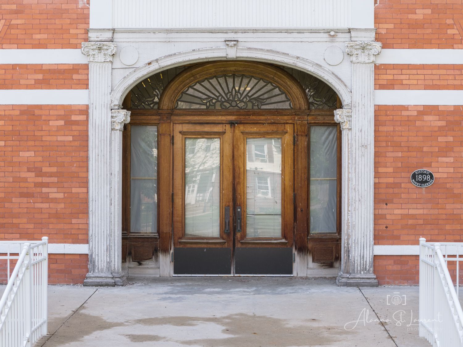 Elegant brick building entrance featuring ornate white stone archway, decorative transom window, and classic wooden double doors.