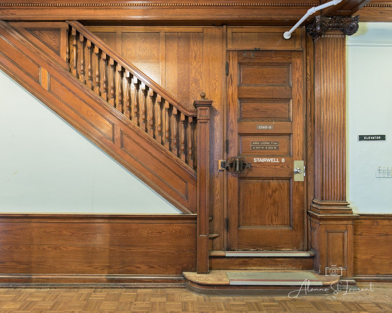 Historic wooden staircase with ornate banister and paneled door in a classic Victorian-style interior.