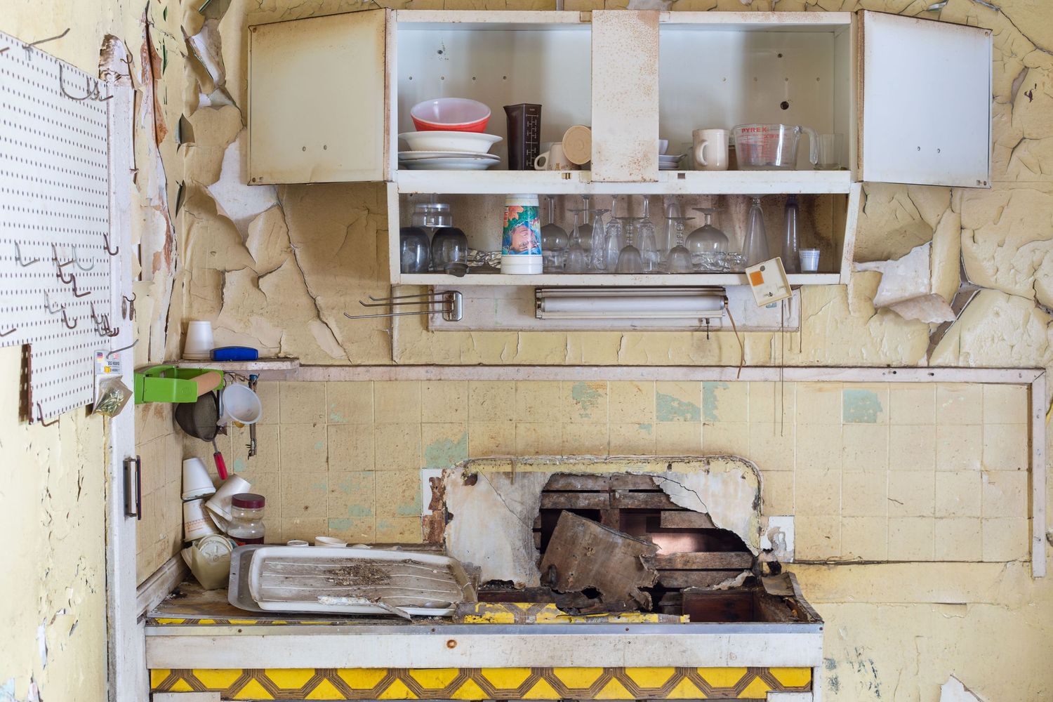 Run-down kitchen with exposed shelving units and peeling paint on walls in a kitchen of an abandoned home in Detroit, Michigan.