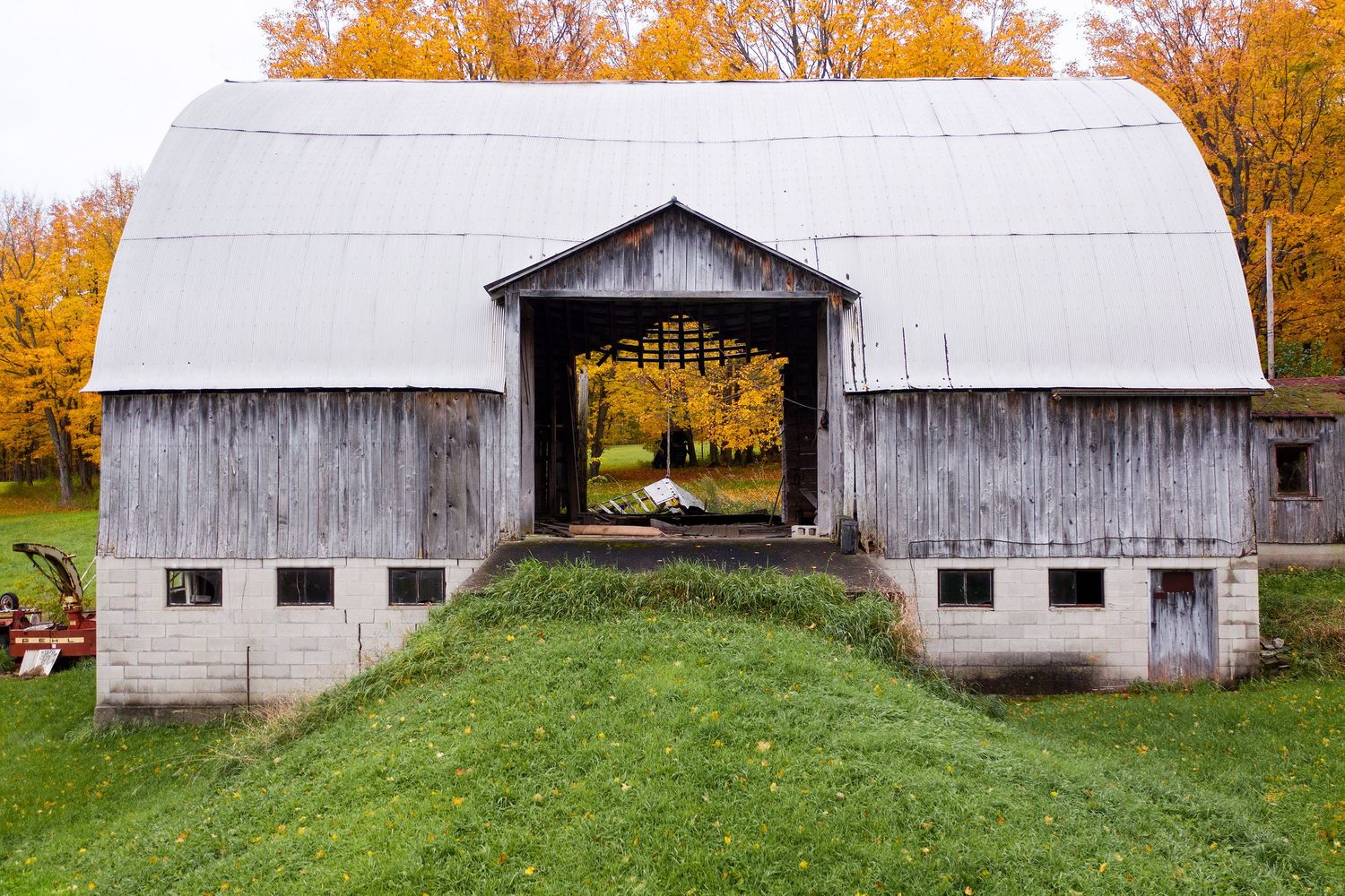 A weathered barn with a metal roof set against vibrant autumn foliage captured with a drone in Michigan.