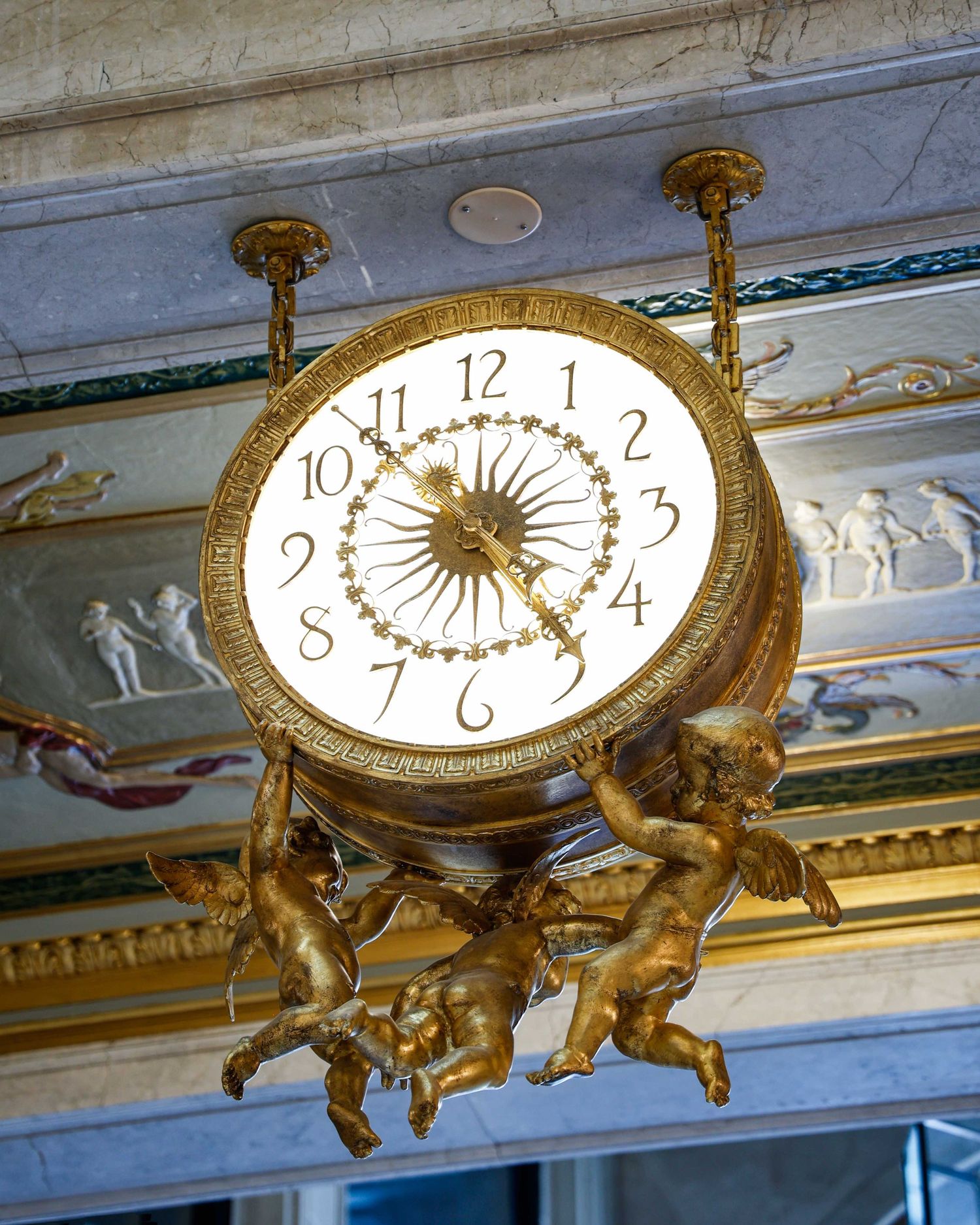 Decorative gold clock with cherub figures mounted on an ornate ceiling in the historic Book Tower lobby in downtown Detroit, Michigan.