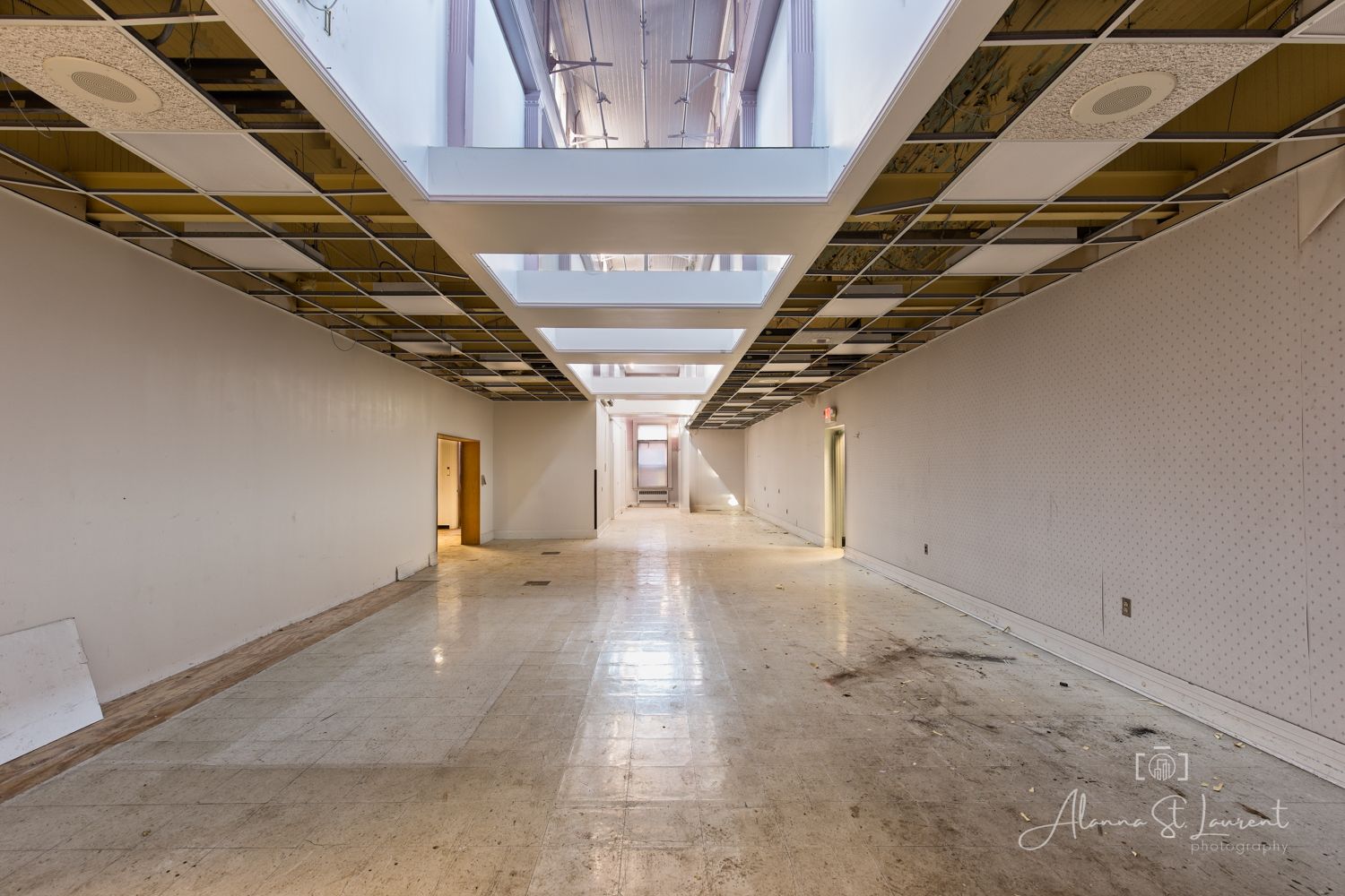 Empty commercial space under renovation with marble floors, exposed ceiling grid, and long hallway with natural light.