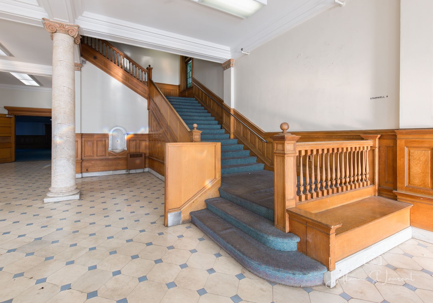 Grand foyer featuring a wooden staircase with blue carpet, ornate balustrade, white columns, and classic wainscoting paneling.